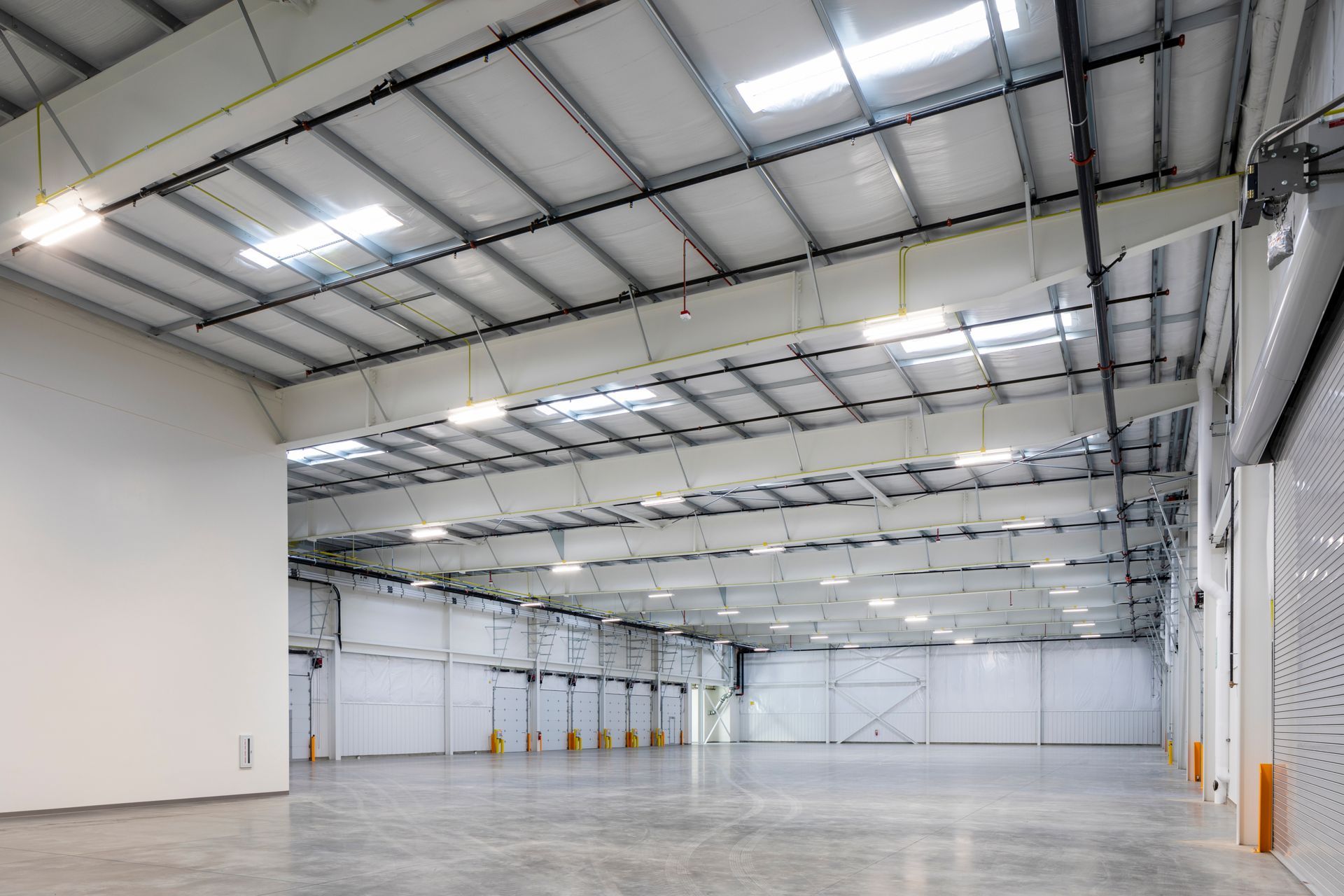 Empty warehouse interior with high white ceiling, concrete floor, and bright overhead lights