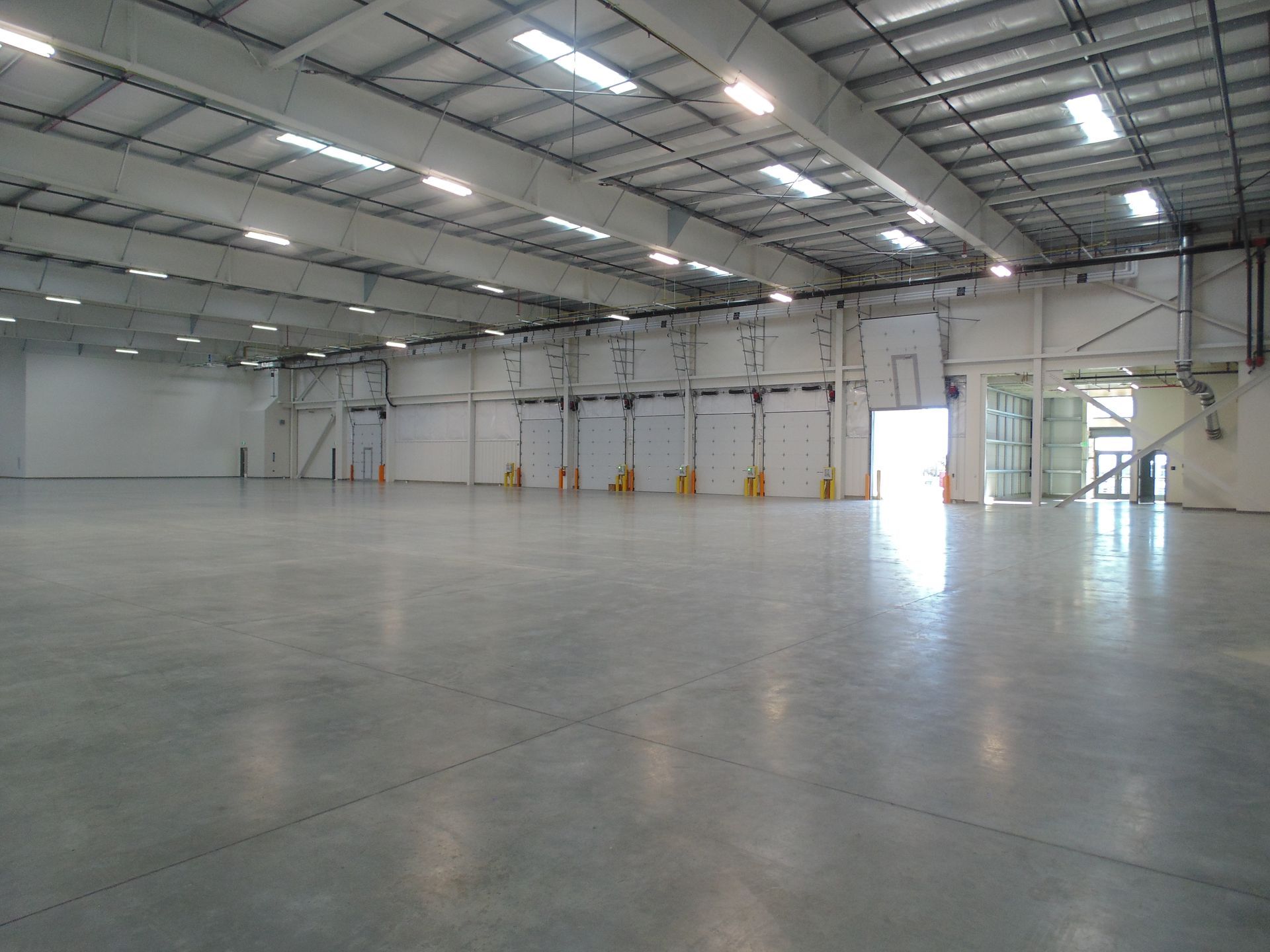 Empty industrial warehouse with a polished concrete floor, white walls, and skylights overhead