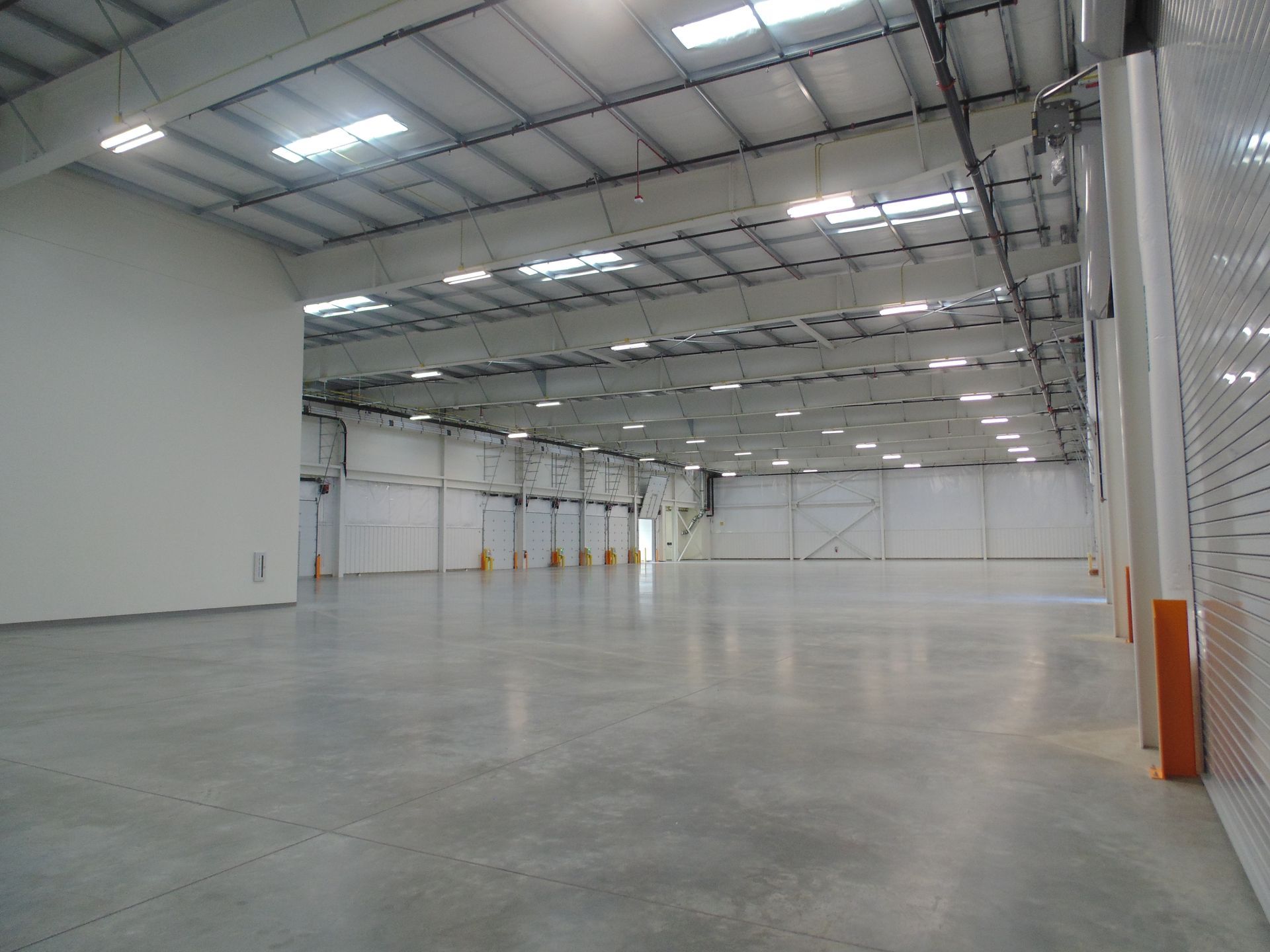 Empty industrial warehouse with high ceilings, white walls, and a polished concrete floor