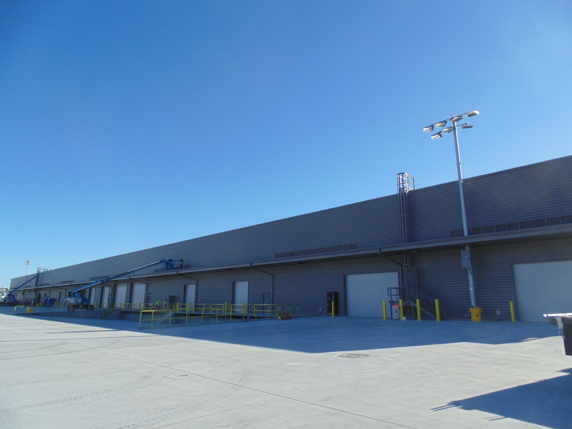 Large industrial warehouse with a long sloped roof and loading docks under a clear blue sky
