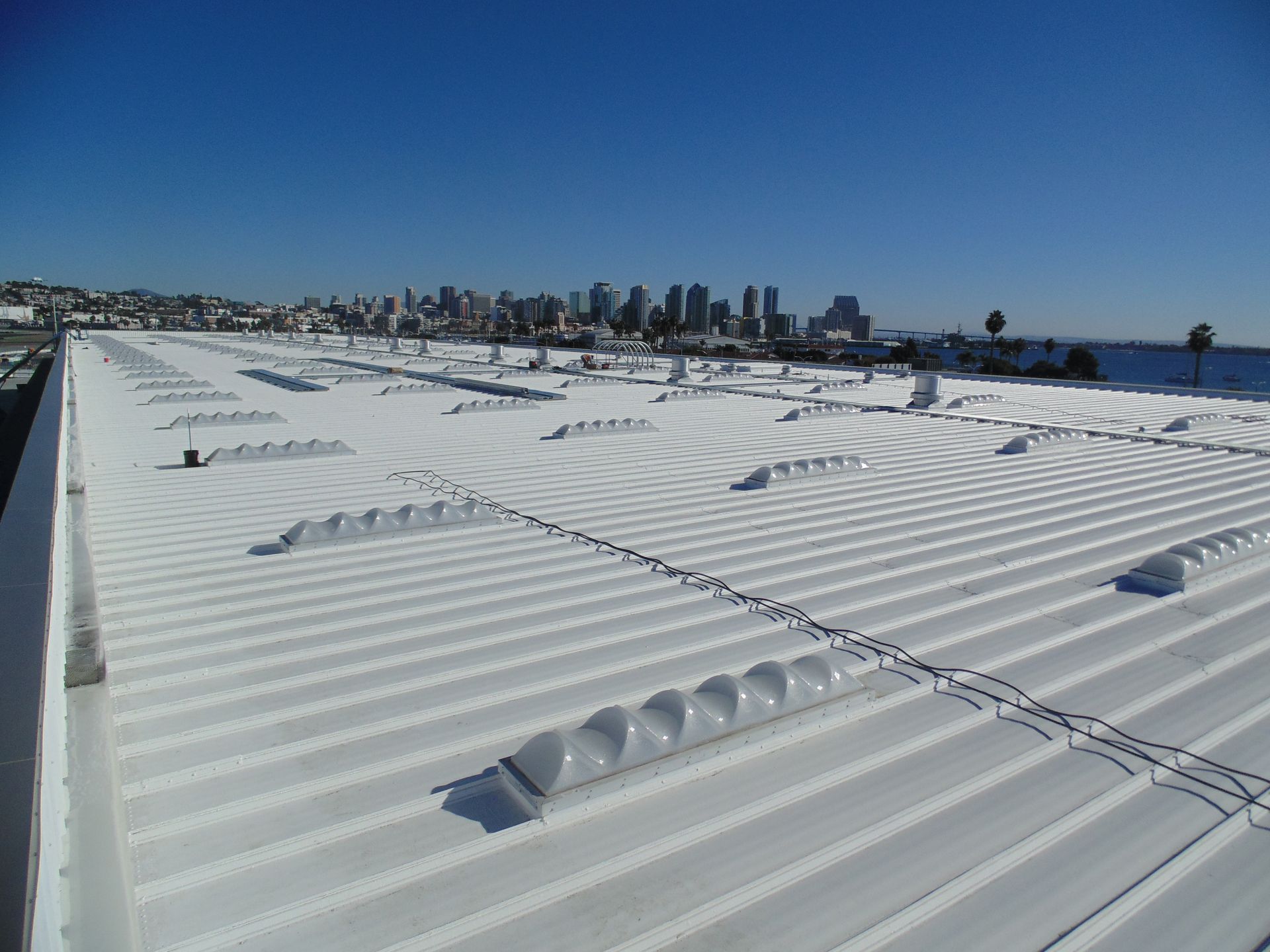 Snow-covered rooftop with rippled drifts and a distant city skyline under a clear blue sky