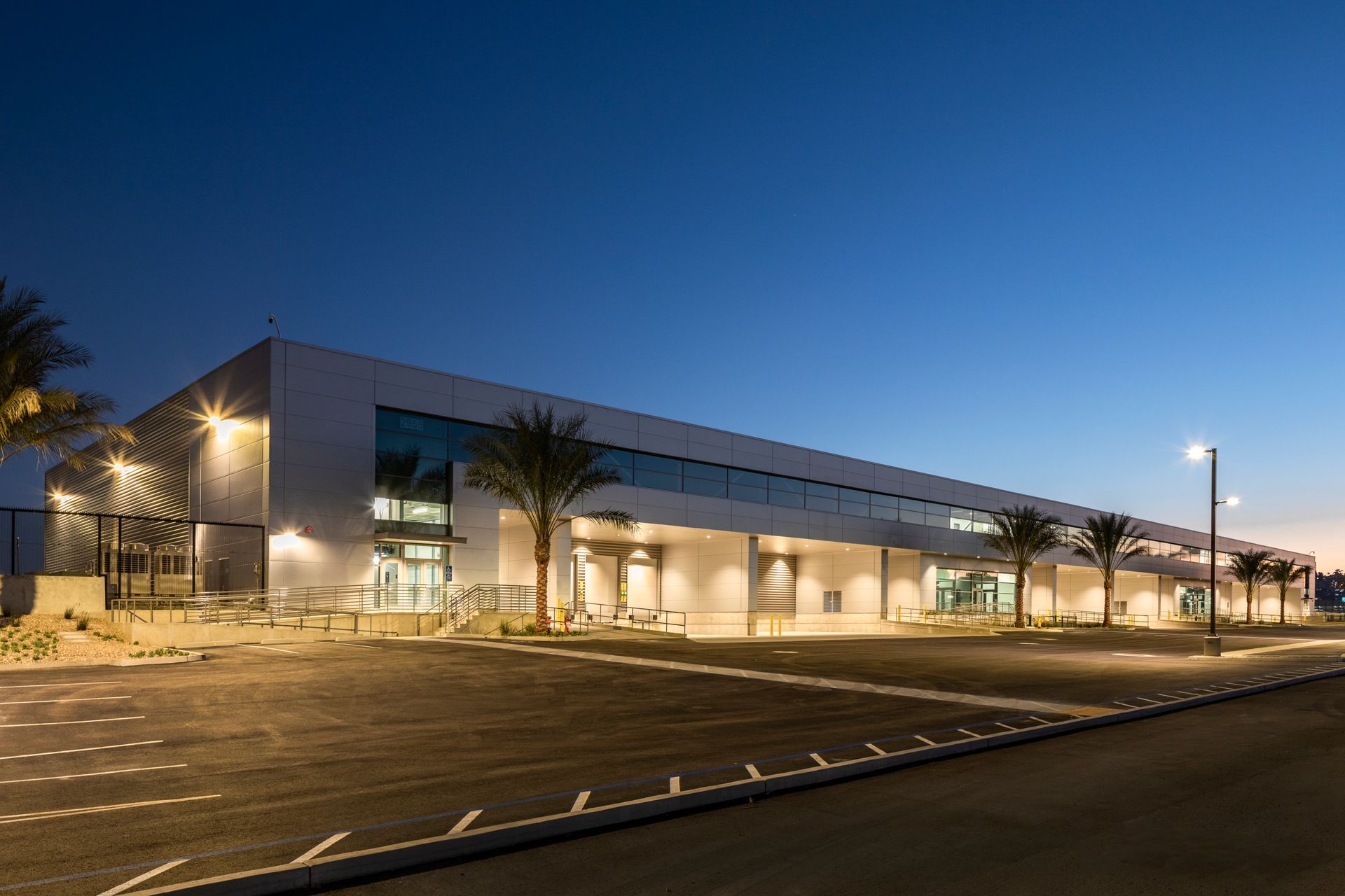 Modern building exterior at dusk with illuminated entrance and empty parking lot