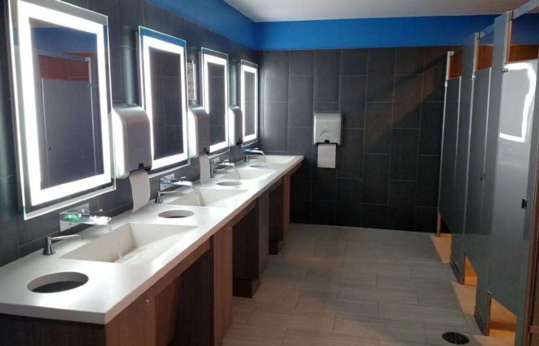 Modern restroom with row of sinks, mirrors, and stalls in blue and black tones