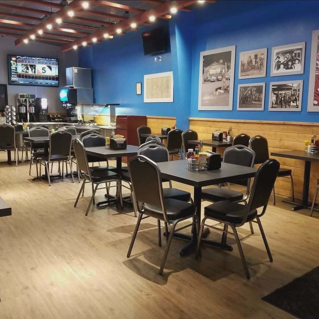 Quiet restaurant dining area with black tables and chairs, blue walls, framed art, and a TV near the counter.