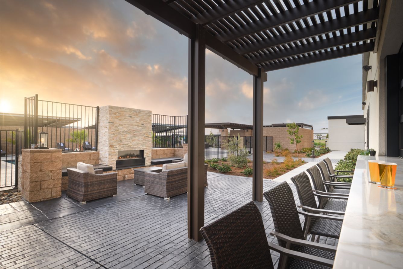 Outdoor rooftop lounge with wicker seating, bar stools, and a sunset view