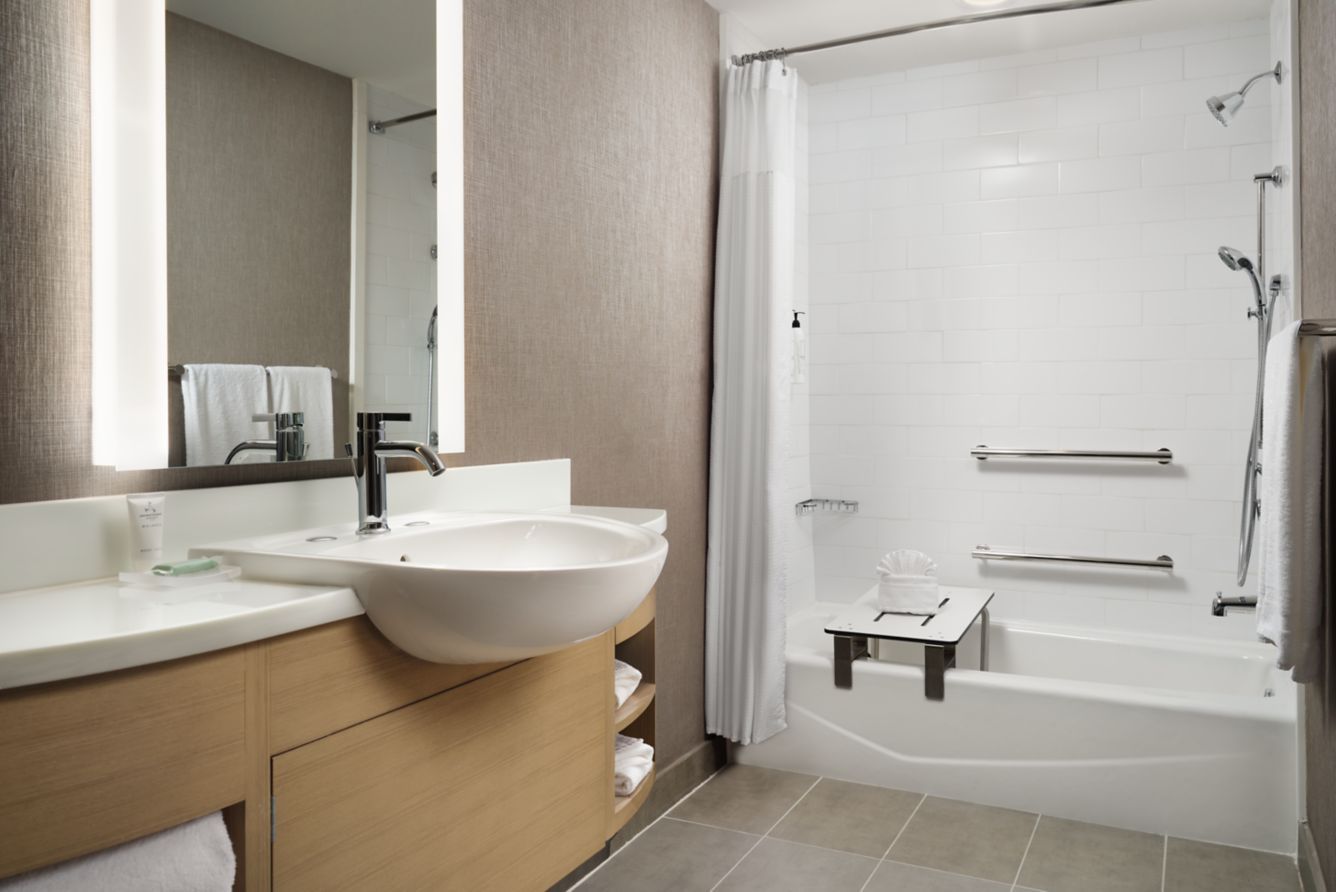 Modern bathroom with vanity sink, mirror, and white shower/tub combo with grab bars