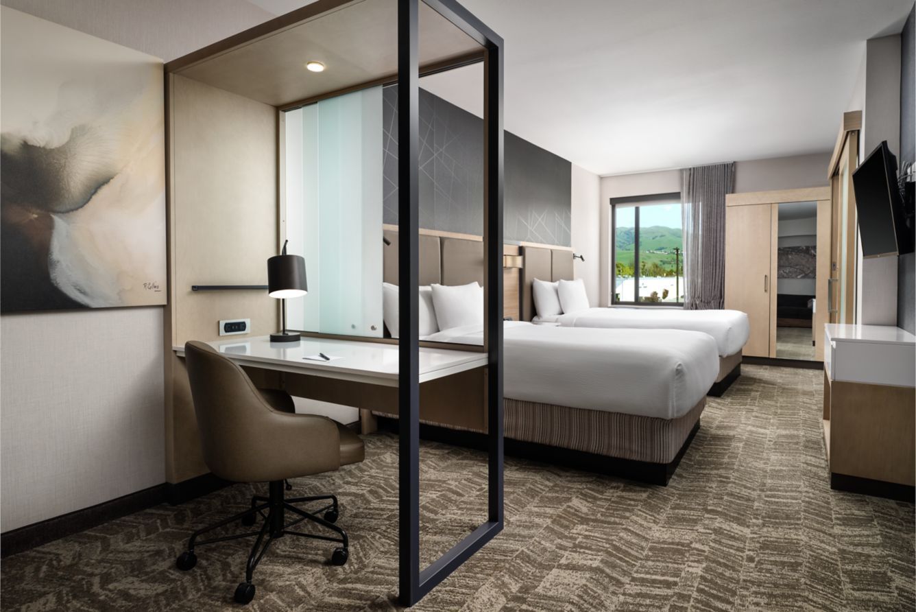 Modern hotel room with bed, desk, chair, large window, and mirrored partition