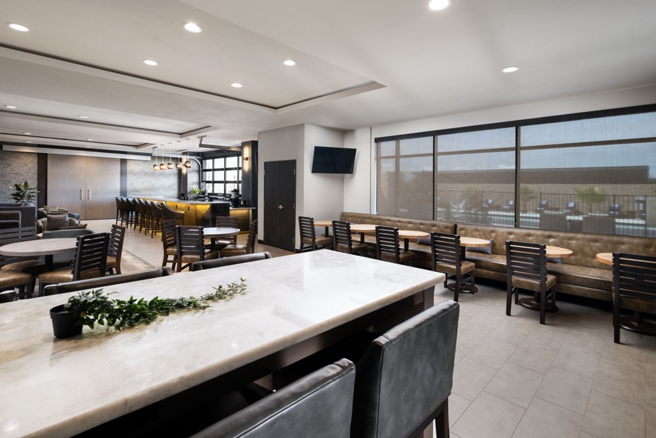 Modern dining room with large windows, wooden tables, chairs, and a marble-top counter