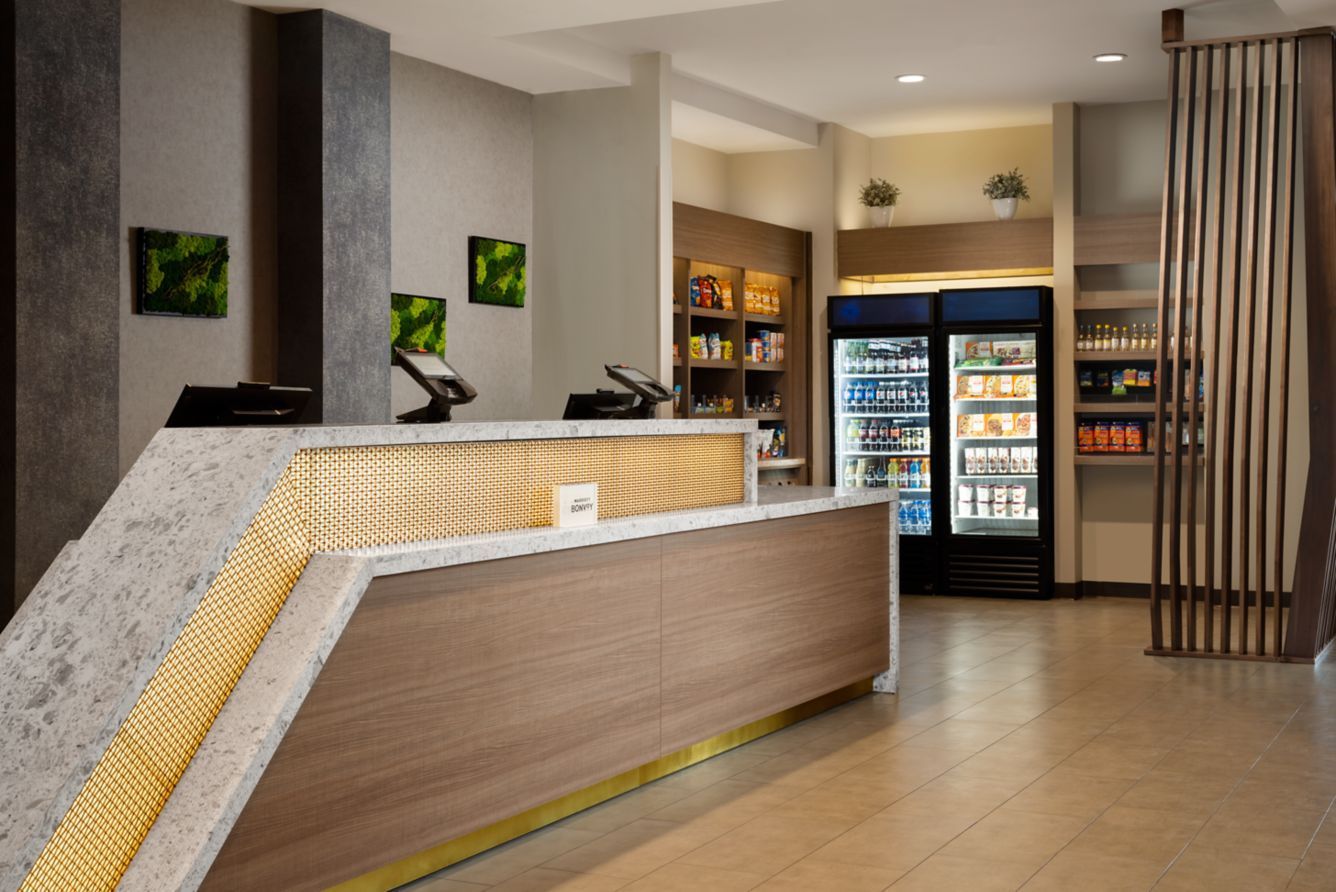 Modern hotel lobby with curved front desk, beverage coolers, and wood-paneled decor