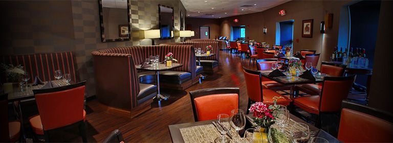 Cozy restaurant dining room with red chairs, set tables, and warm ambient lighting