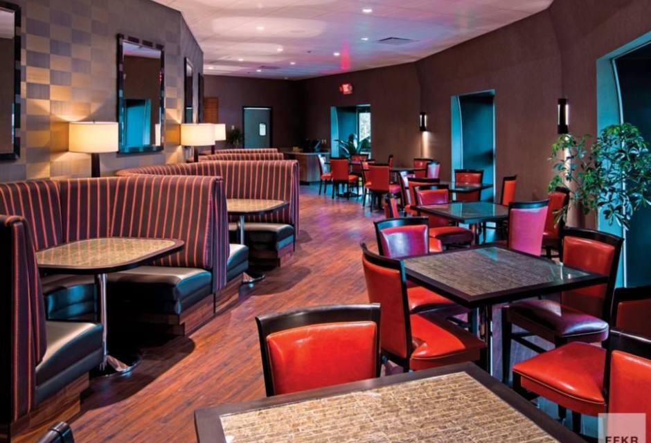 Empty restaurant dining area with red chairs, booth seating, and patterned carpet