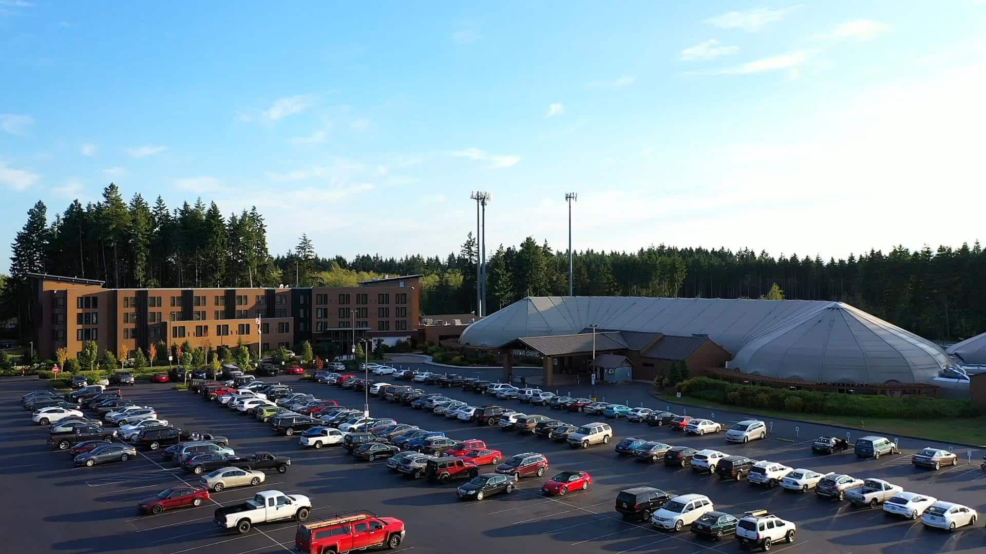 Parking lot full of cars beside a building and large tent under a blue sky
