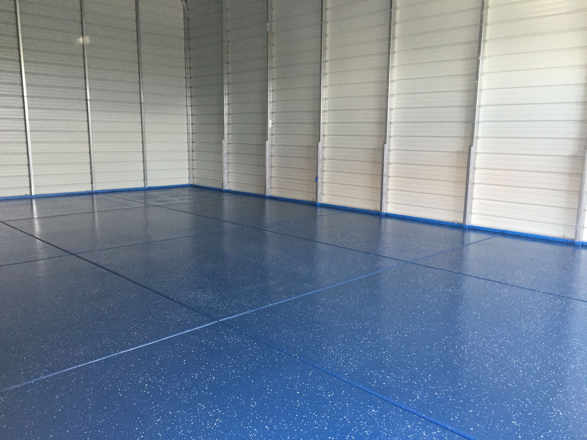 Empty garage with blue speckled floor and white walls, viewed from a corner.