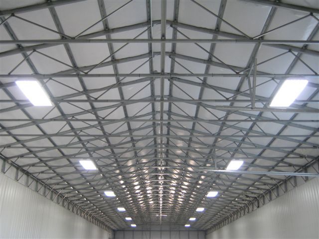 Interior of a large warehouse with a high metal truss ceiling and rows of overhead lights