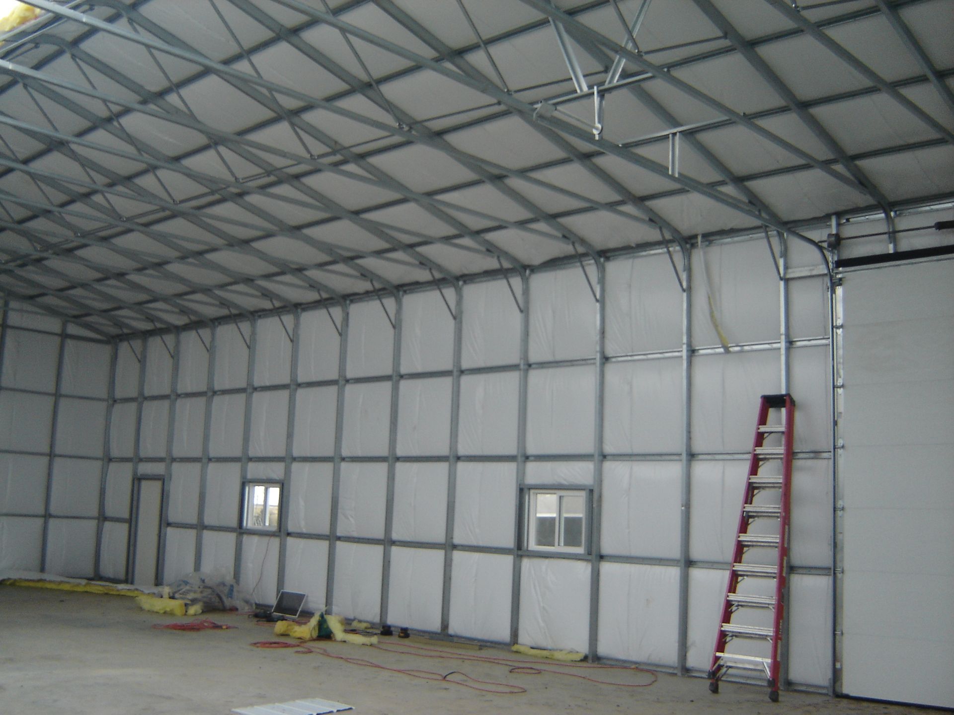 Empty warehouse interior with metal wall panels, windows, and a red ladder leaning against the wall.