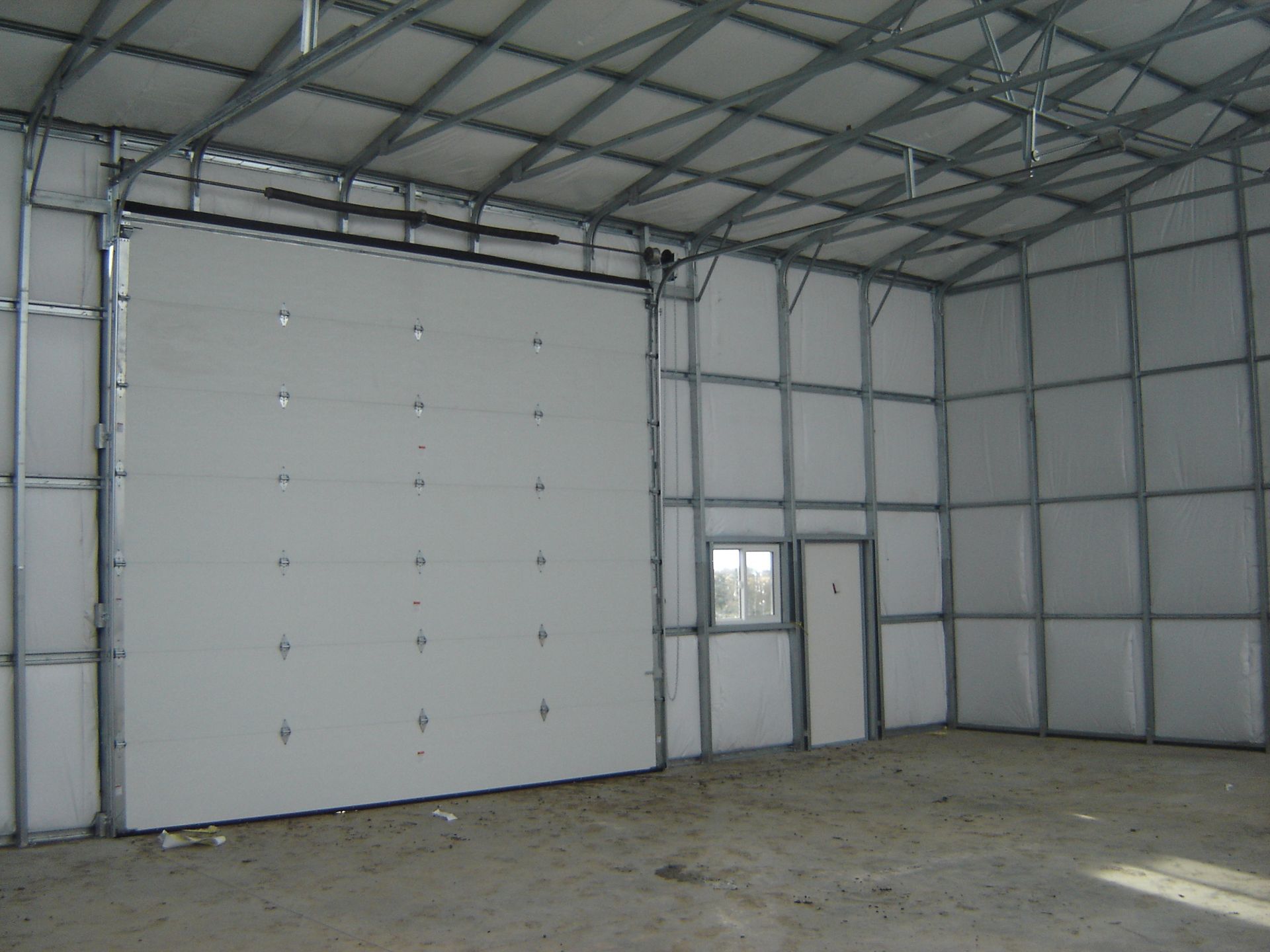 Empty metal warehouse interior with concrete floor and large white roll-up door