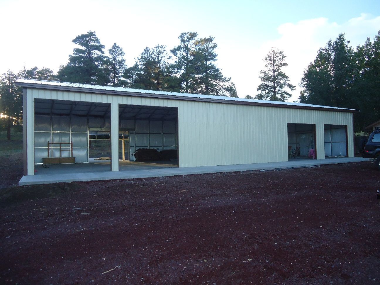 Single-story metal building with large windows and an open bay, surrounded by trees.
