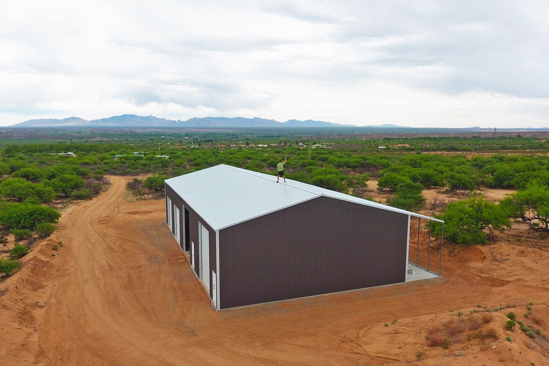 Small metal shed on a dirt road in a rural landscape with distant mountains and cloudy sky