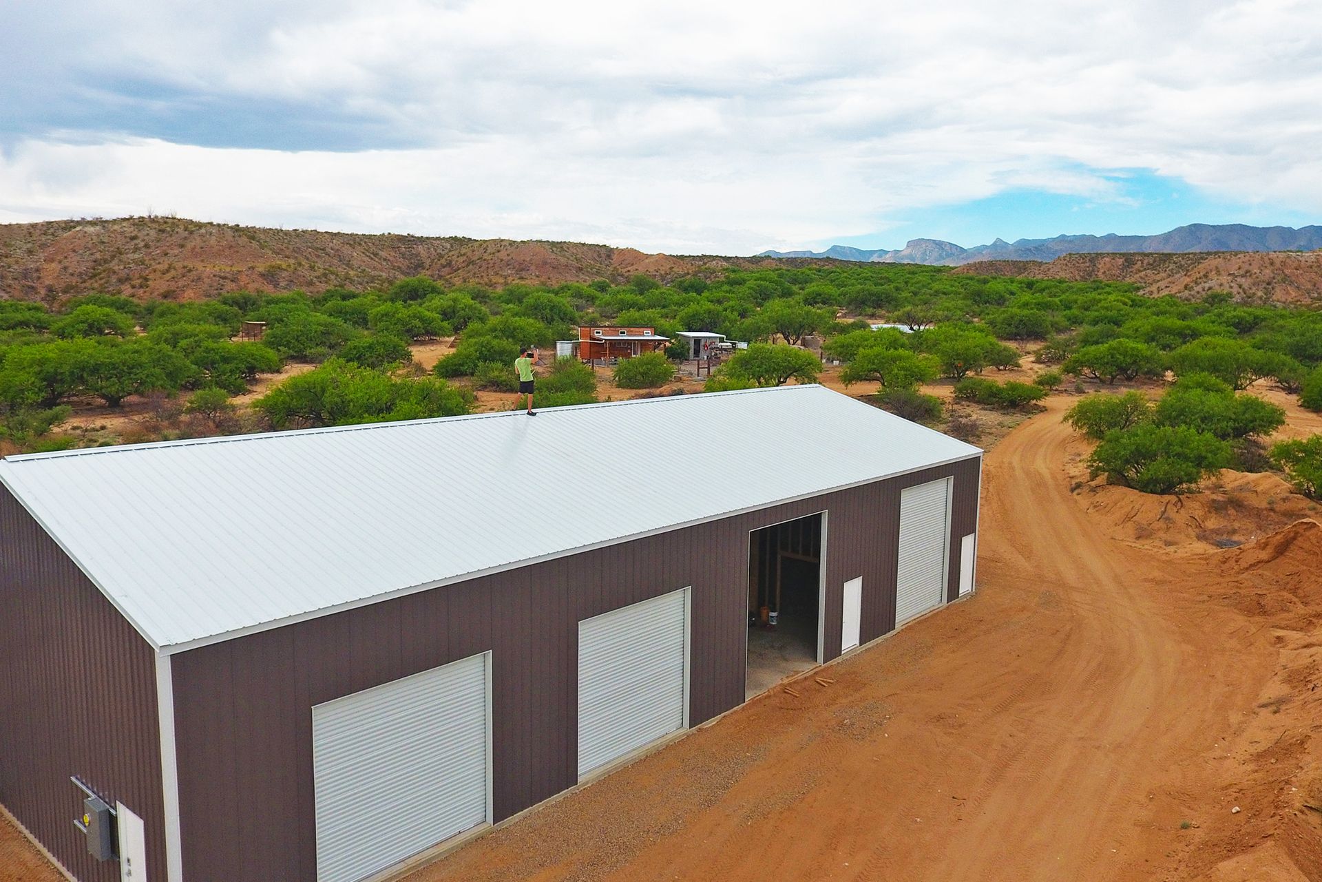 Single-story metal warehouse with white roof on a dirt lot in a desert landscape