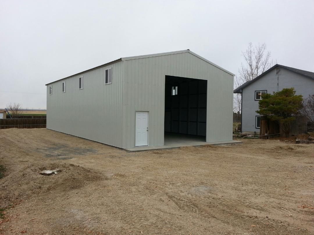 Large gray metal storage building with an open front on a dirt lot under an overcast sky
