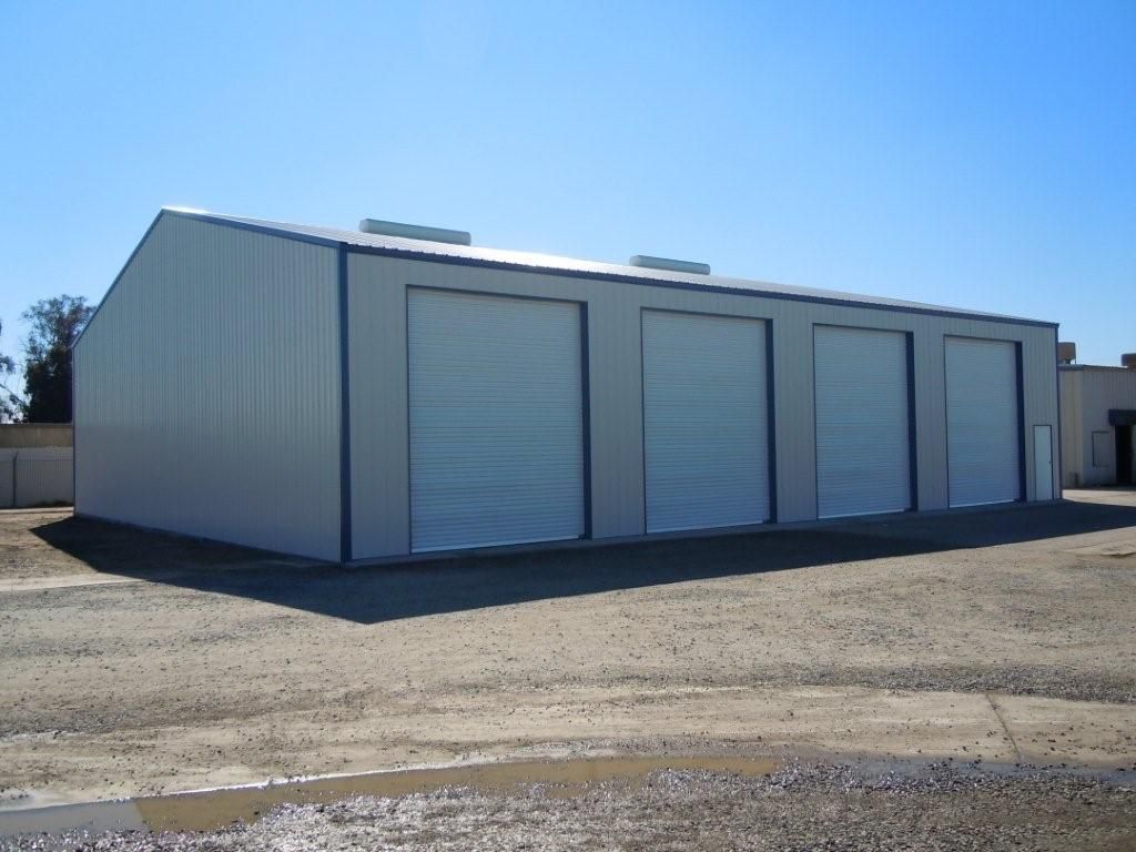 Row of white industrial storage units with closed doors on a gravel lot under a blue sky
