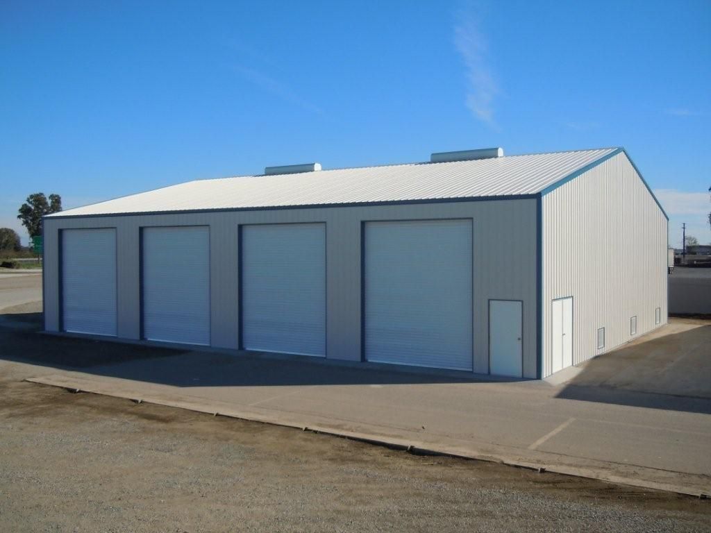 White metal storage building with four roll-up doors and a side entry on a paved lot