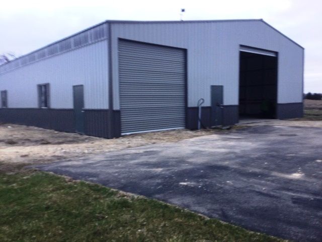 Large gray metal warehouse with two garage doors on a paved lot under an overcast sky