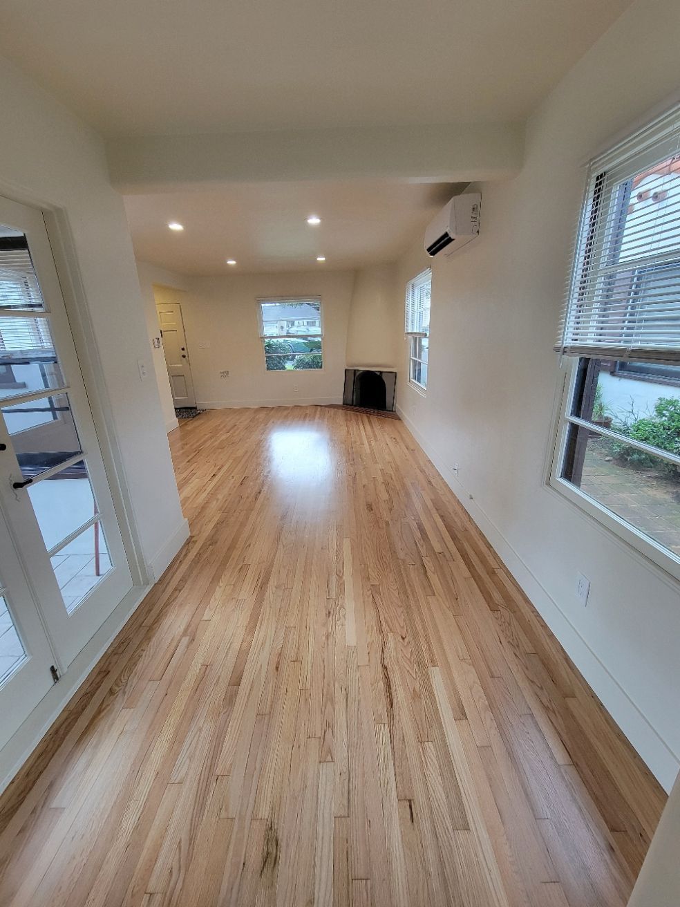 Empty bright room with hardwood floors, white walls, recessed lights, and windows on both sides.