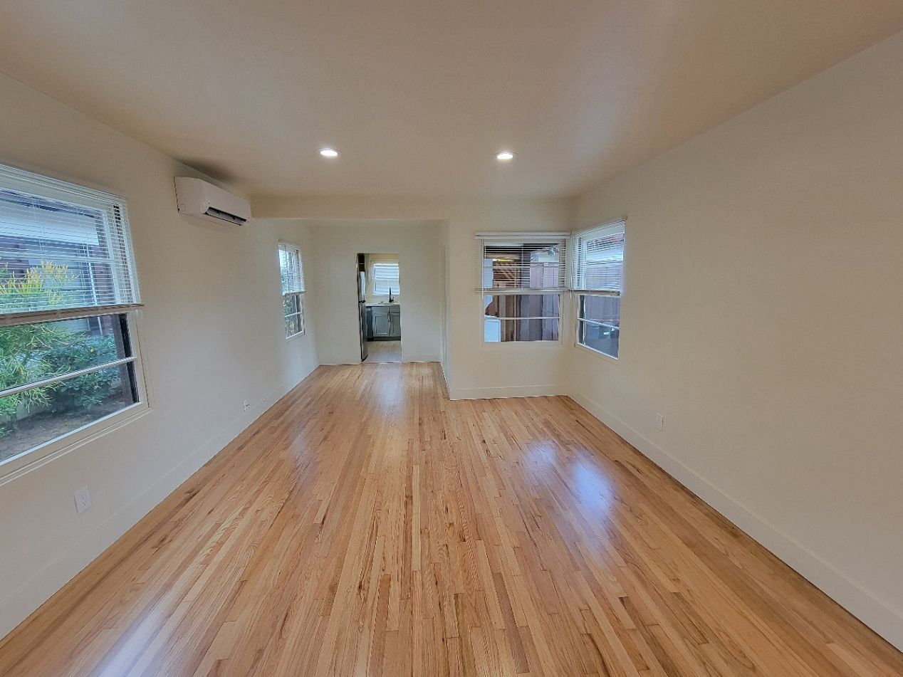 Empty bright room with wood floors, white walls, recessed lights, and windows on both sides.