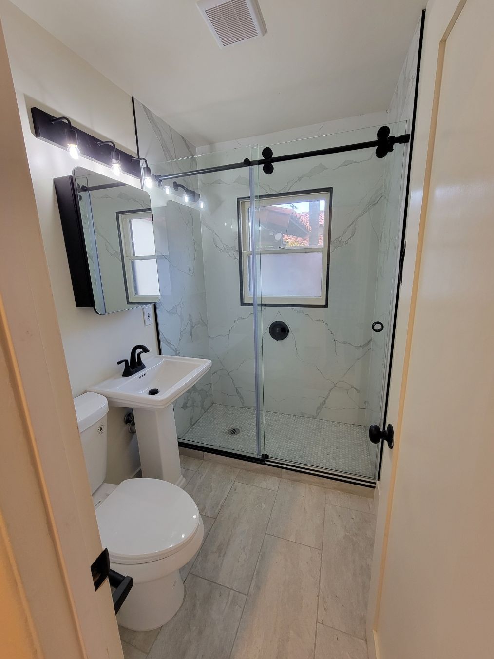 Small bathroom with pedestal sink, toilet, and glass shower enclosure with frosted window.
