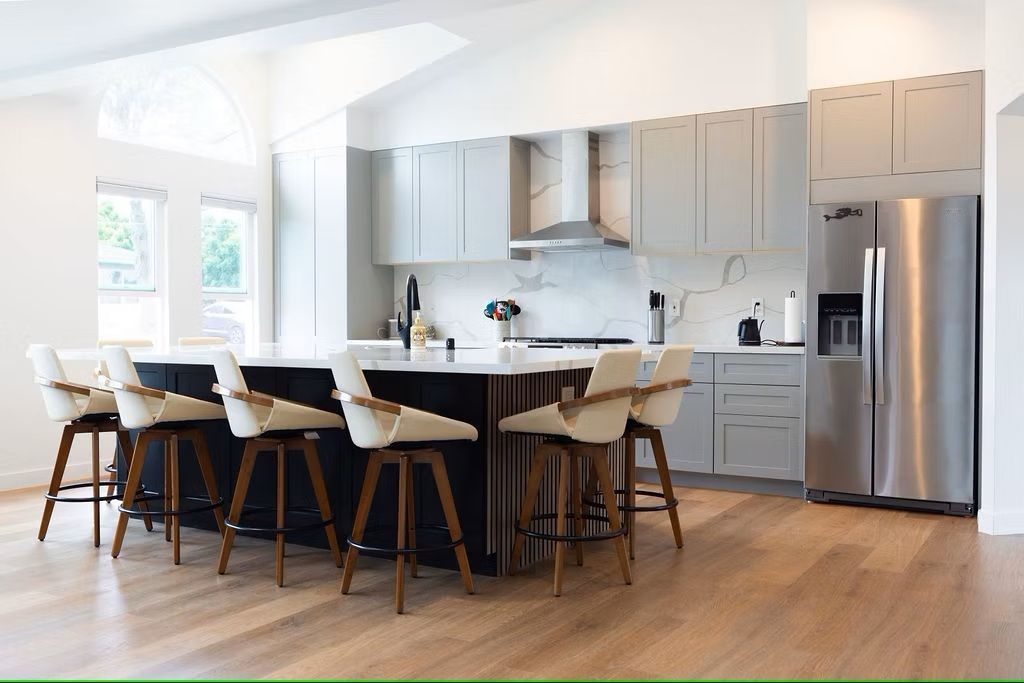 Modern kitchen with a large island, stainless steel appliances, light wood floors, and gray cabinets.