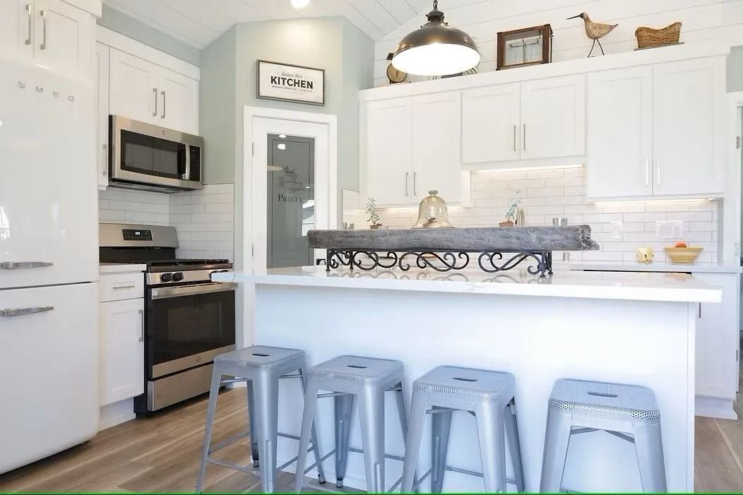 White kitchen with stainless steel appliances, white cabinets, island with stools, and light blue walls.
