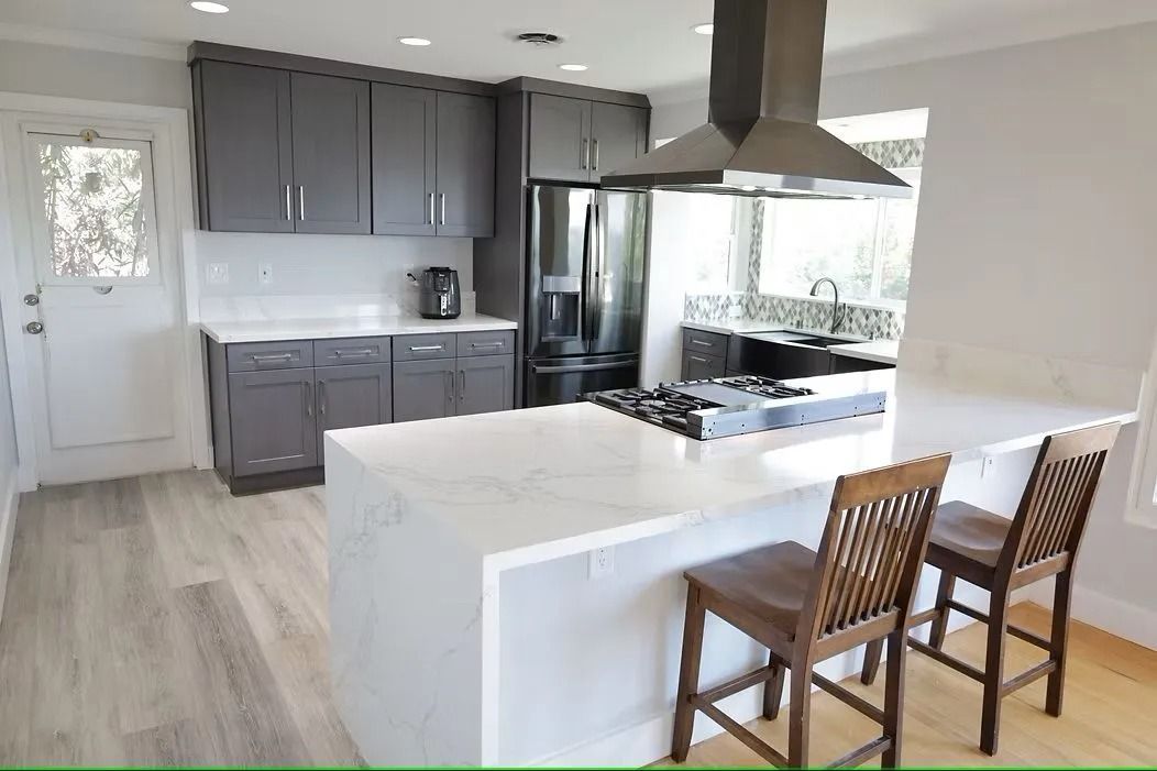 Modern kitchen with gray cabinets, white island, and wooden chairs.