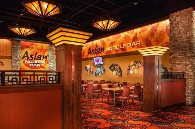 Asian noodle bar interior with tables, red carpet, decorative lighting, and orange walls.