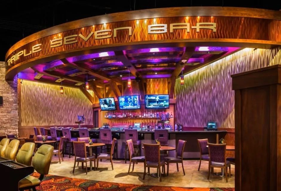 Bar with purple lighting, wood accents, televisions, and seating.