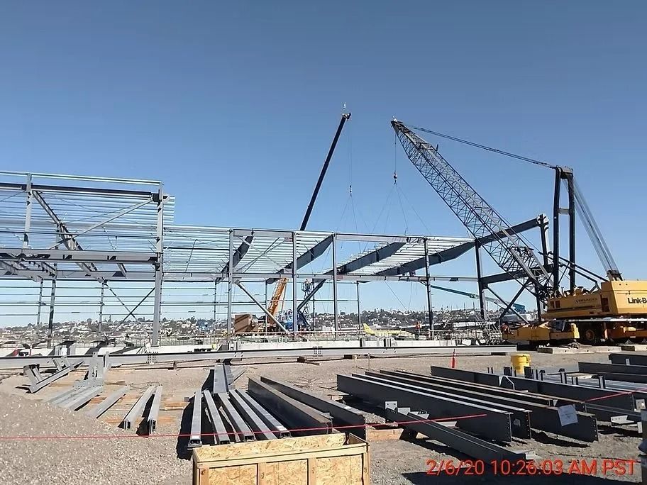 Construction site with steel framework and cranes under a blue sky.