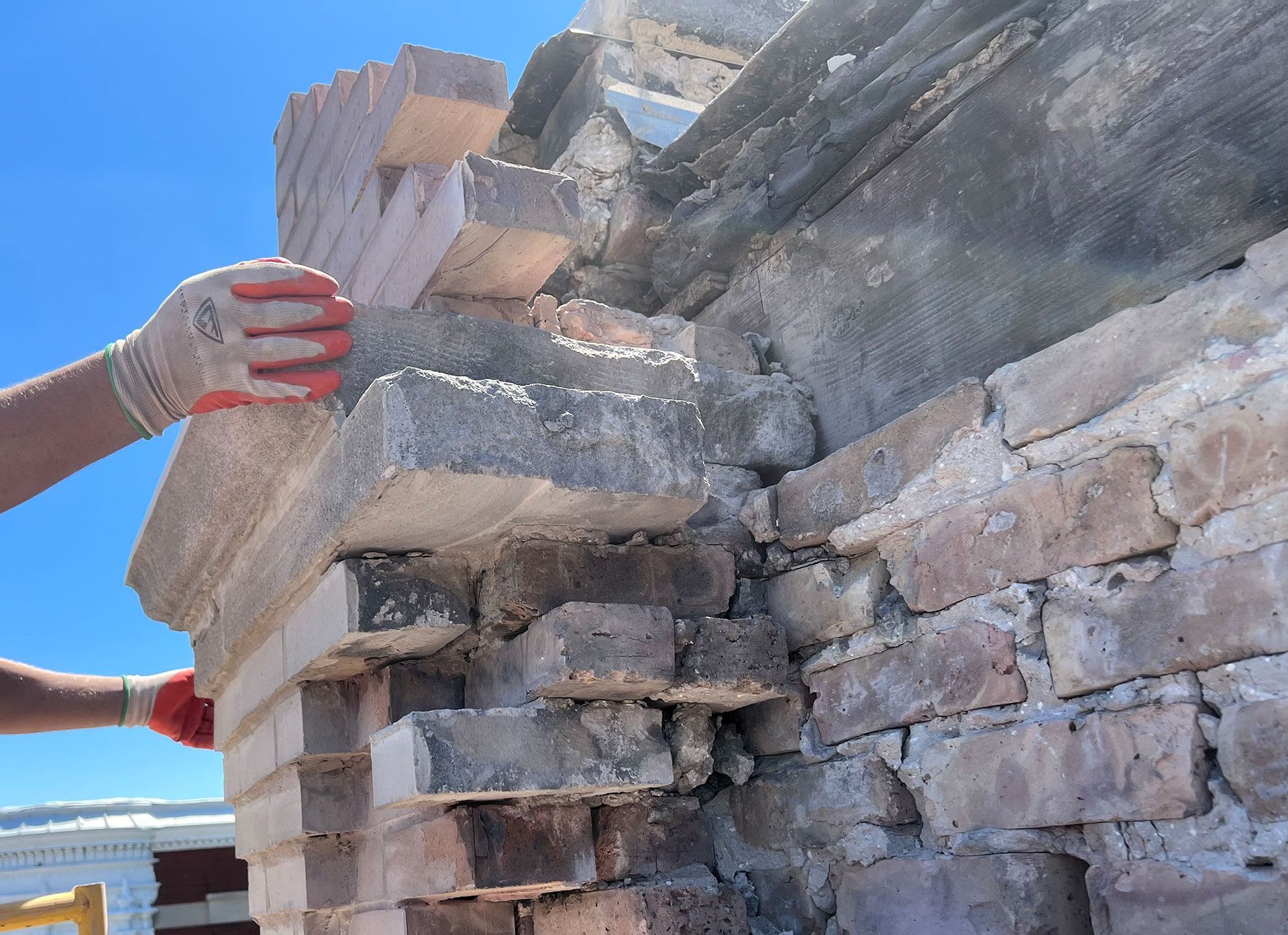 Gloved hands stacking rough stone blocks against a clear blue sky
