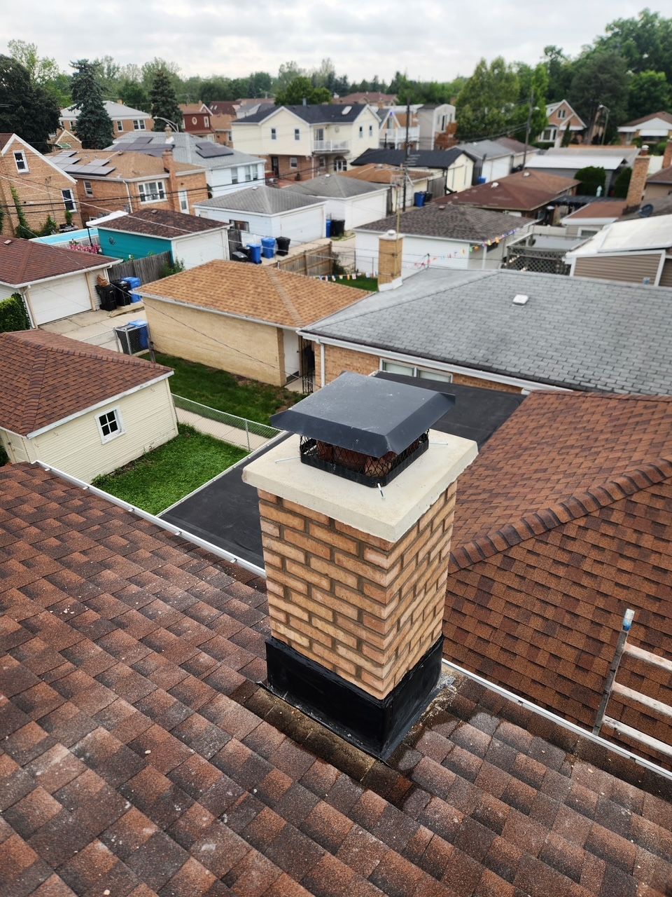 Rooftop view over suburban houses with a brick chimney in the foreground, under cloudy skies.