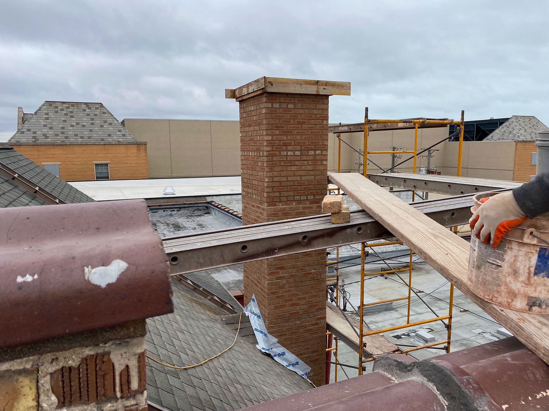 Roof construction site with brick chimney, metal scaffolding, and workers on a partially built roof