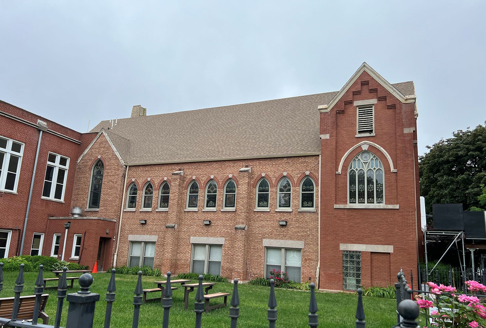 Brick church building with arched windows, red doors, and green lawn under a cloudy sky