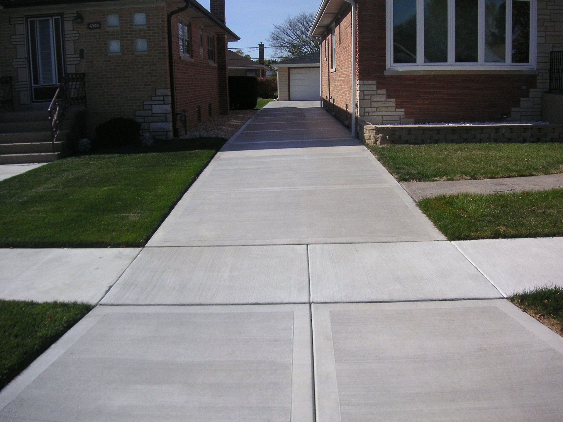 Concrete sidewalk path between brick buildings leading to a sunny courtyard