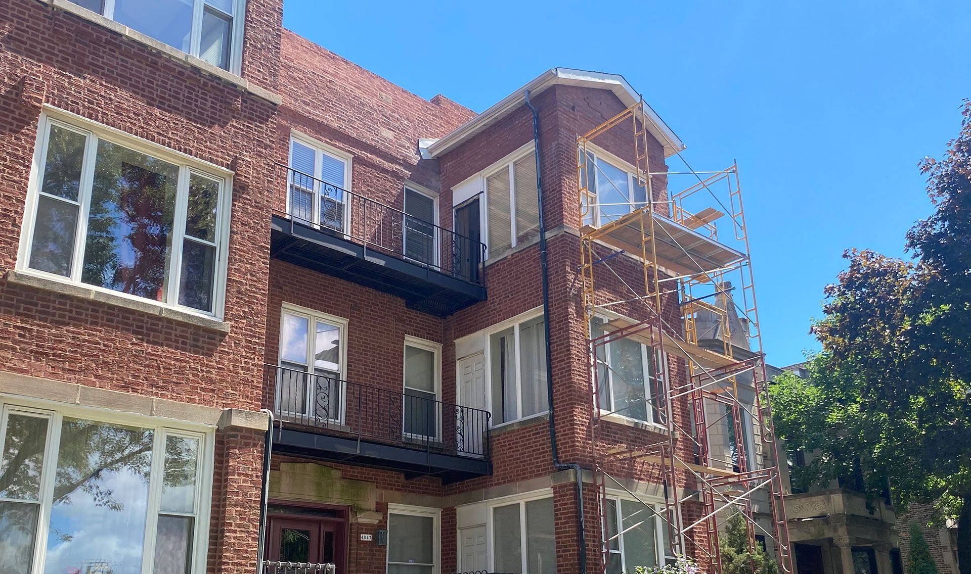Brick apartment building with balconies and scaffolding under a clear blue sky
