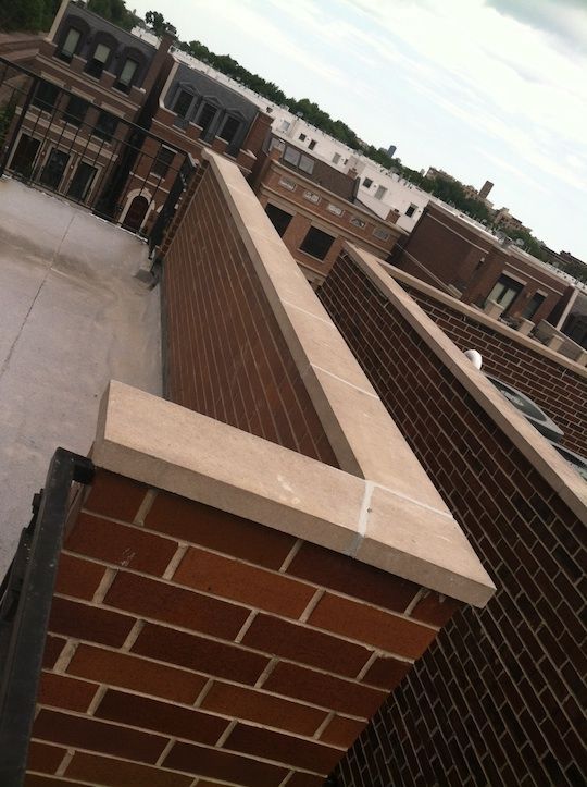 Rooftop walkway with brick walls and white trim, viewed at an angle over nearby buildings.