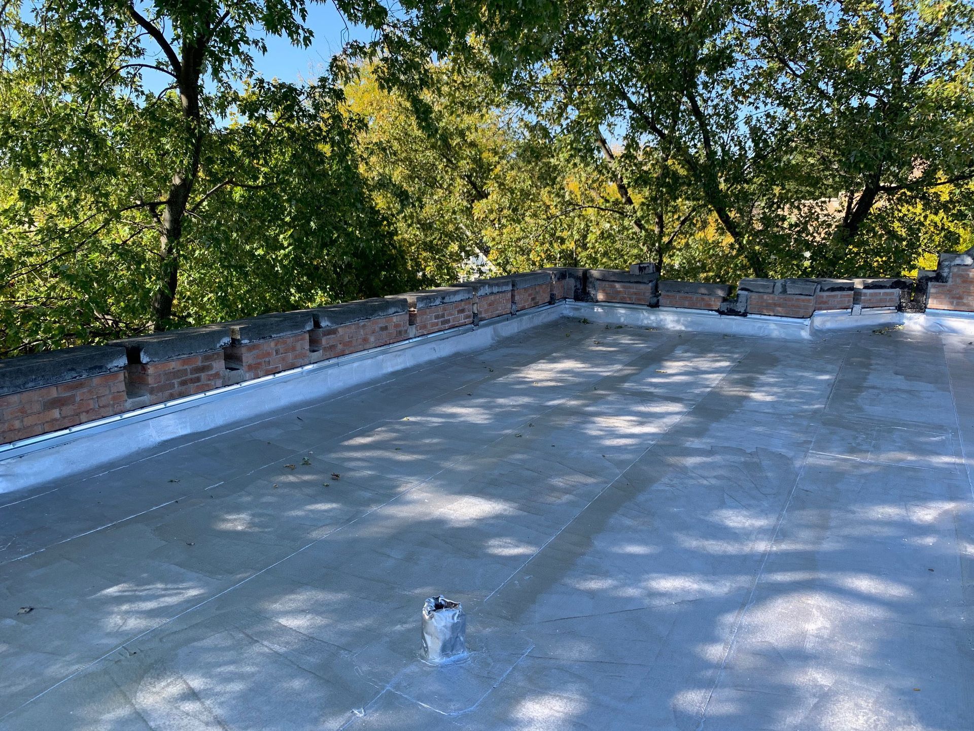 Flat rooftop with white membrane, brick parapet, and trees in the background.