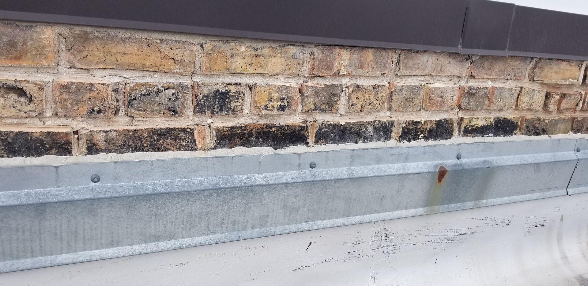 Close-up of a brick wall with a gray metal ledge and weathered white base below.