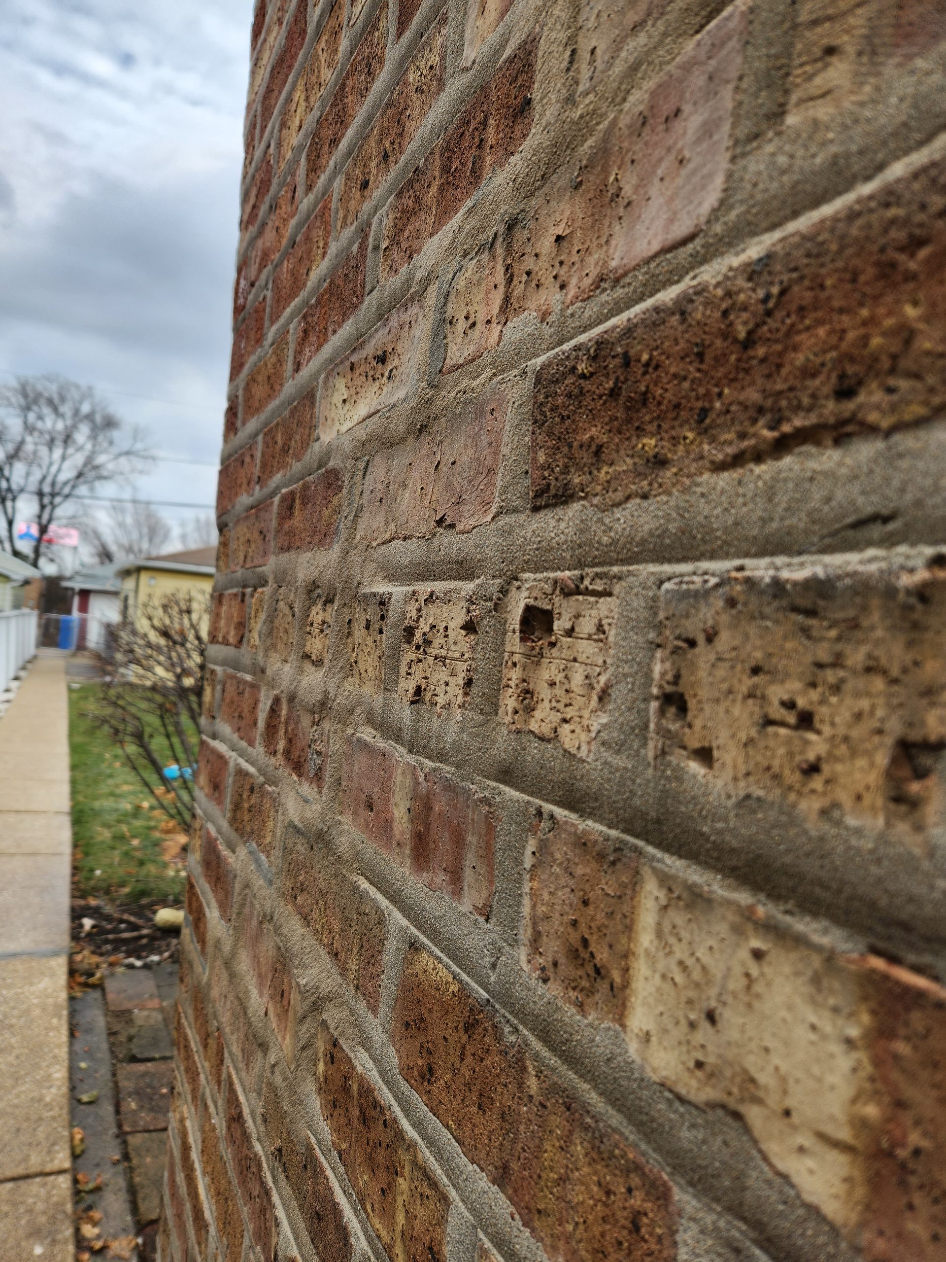 Close-up of a brick wall beside a sidewalk, with a building and cloudy sky in the background