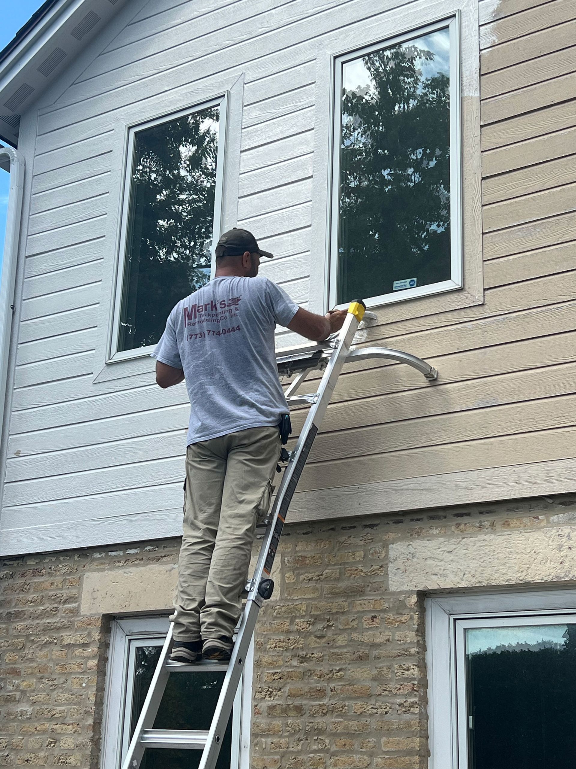 Worker on a ladder painting the exterior siding of a house between windows