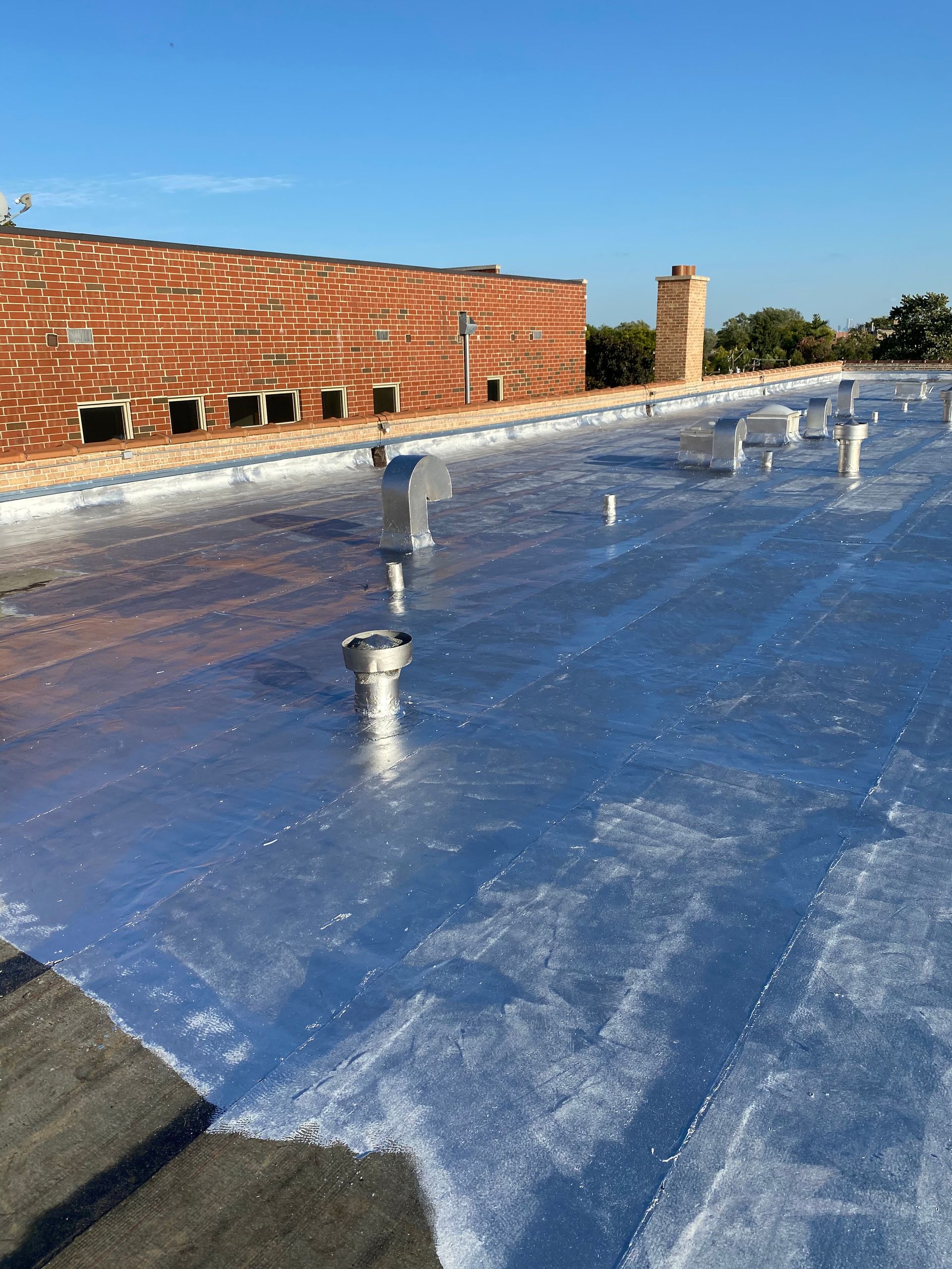 Rooftop covered in reflective blue waterproofing under a clear sky, with brick walls and vent pipes.