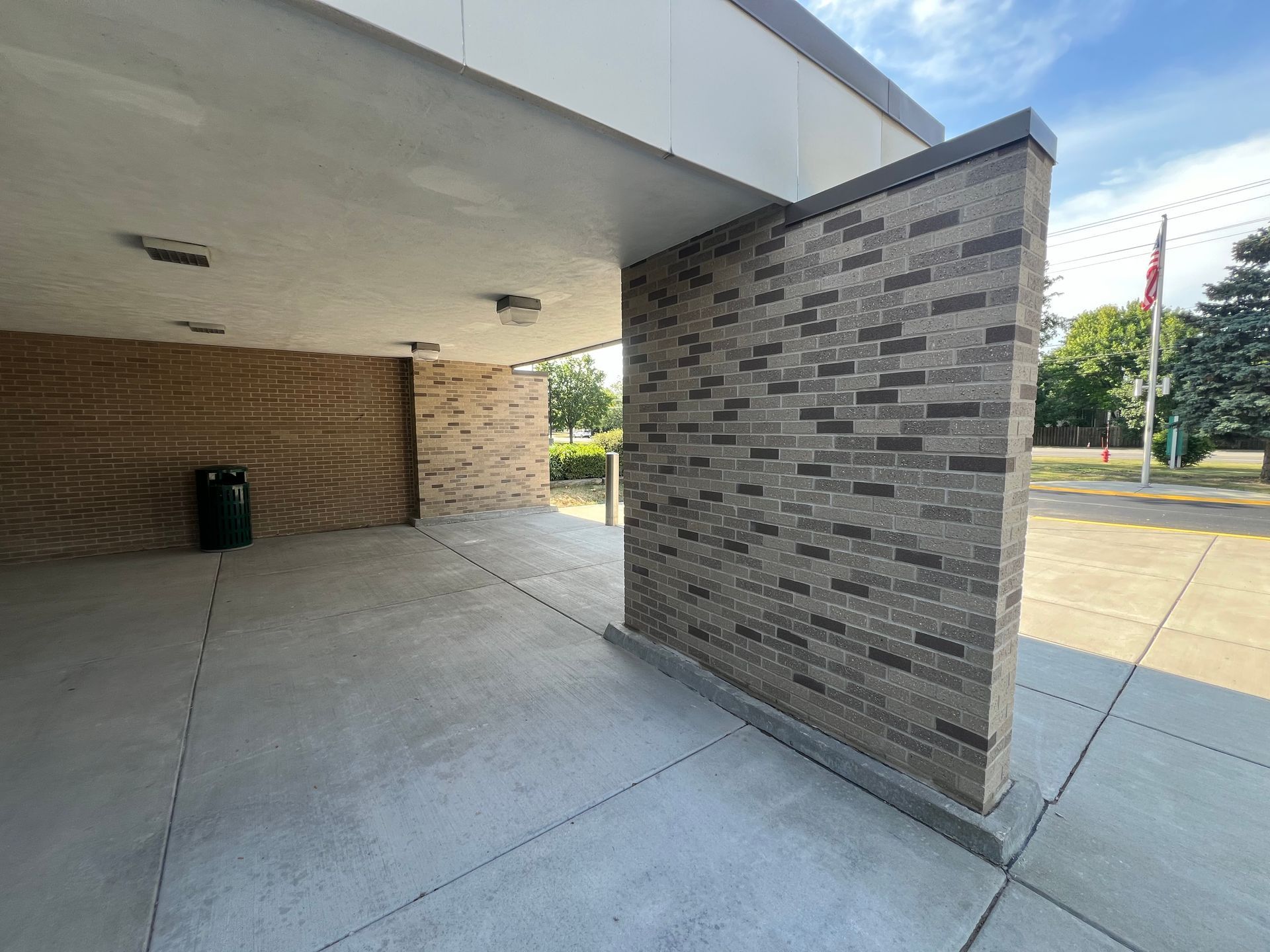 Covered outdoor walkway beside a brick building with tiled wall and concrete floor
