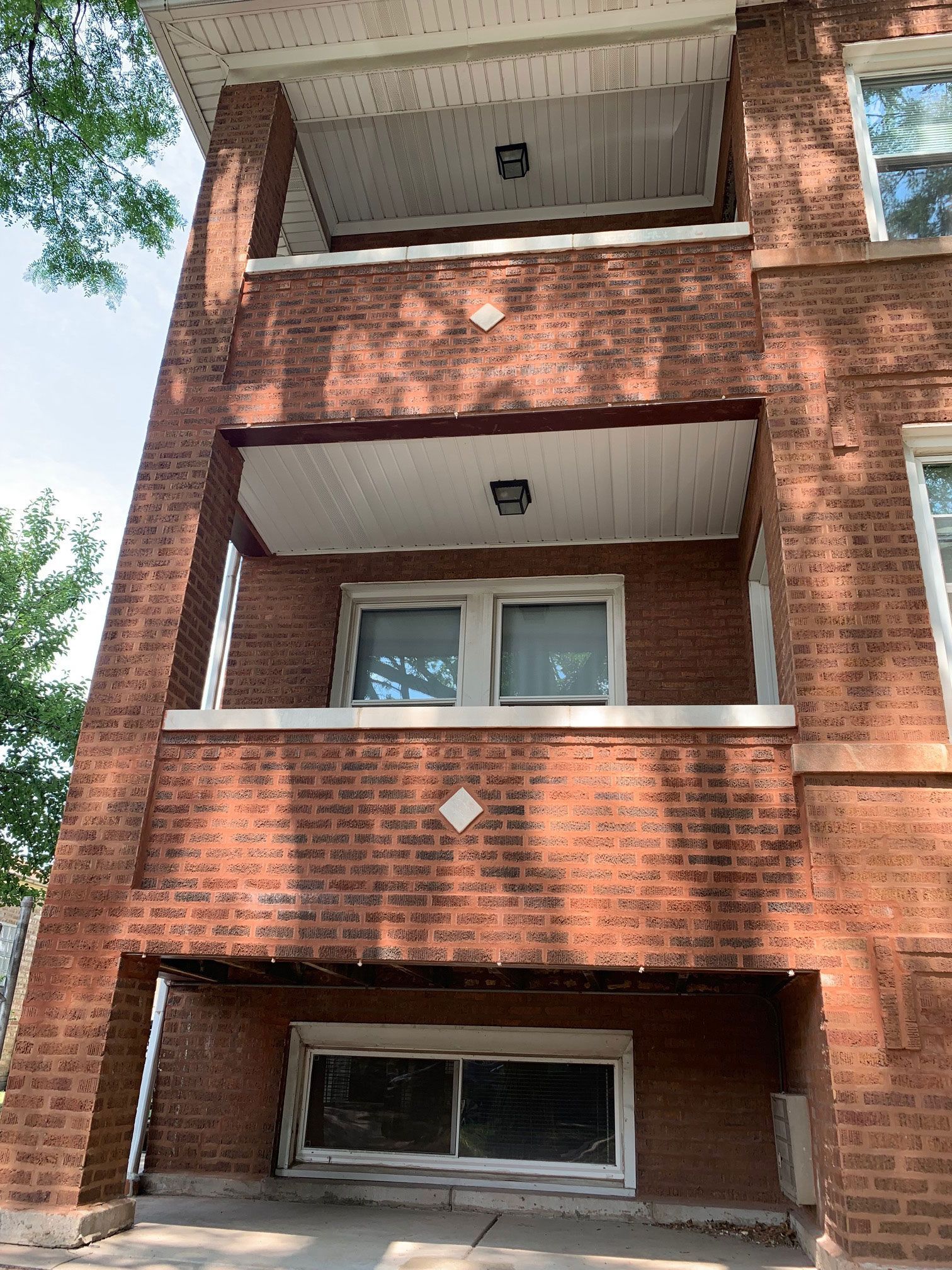 Brick apartment building balconies and windows viewed from below, with trees framing the left side.